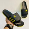 a person holding a black and yellow adidas slides